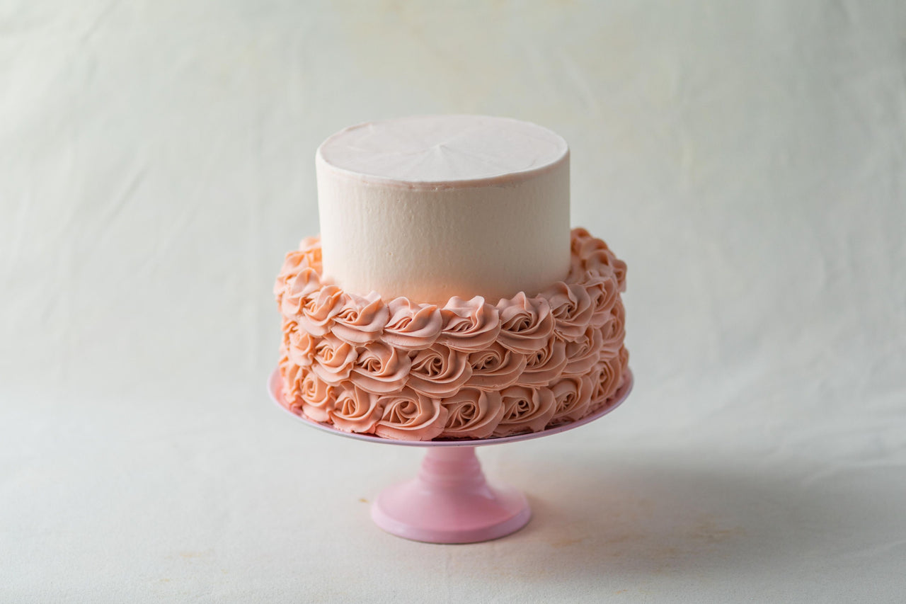 a custom cake decorated with pink rosettes on a pink cake stand