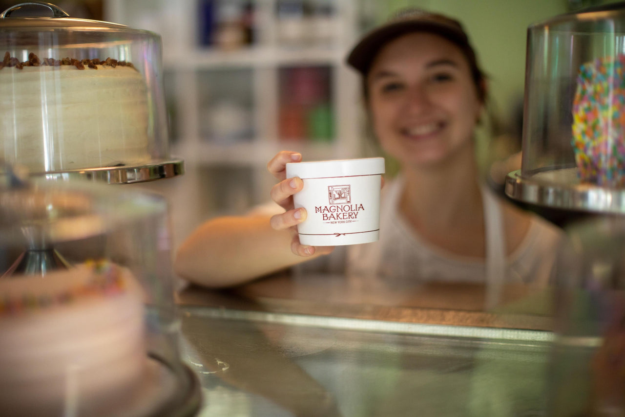a magnolia bakery employee handing a cup of banana pudding from behind a counter