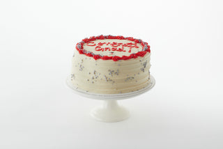 A confetti cake with white and red buttercream decorated with silver confetti and a "Congrats Grad" inscription