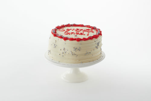 A confetti cake with white and red buttercream decorated with silver confetti and a "Congrats Grad" inscription